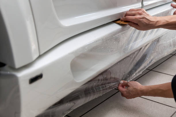 retrofitting o carro com uma película protetora transparente contínua, o mestre cola o revestimento que protege os veículos dos riscos e das microplaquetas na oficina. - retrofitting - fotografias e filmes do acervo