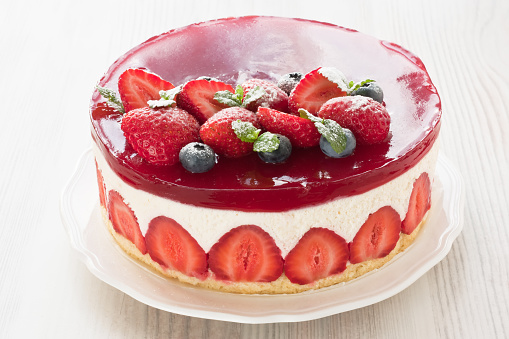 Delicious strawberry cake mousse fraisier decorated fruity jelly glaze, berries and mint on white wooden background