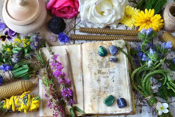 Witch spell book, calendula, rose flowers, reiki crystals and candles on wooden table. Esoteric, occult and mystic concept, alternative medicine background with natural healing ingredients.