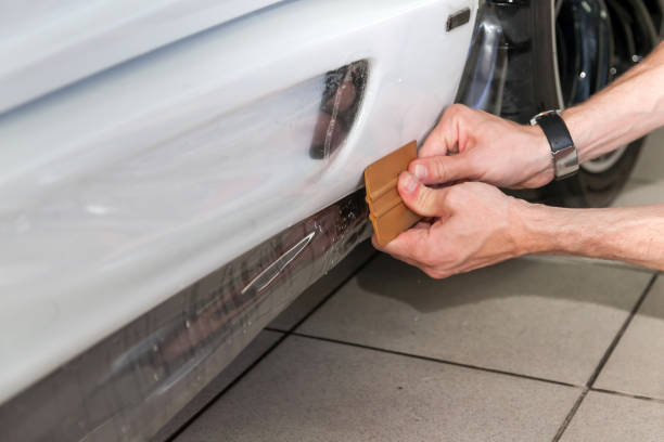 reacondicionando el coche con una sólida película protectora transparente, el maestro pega el recubrimiento protegiendo los vehículos de arañazos y virutas en el taller. - retrofitting fotografías e imágenes de stock