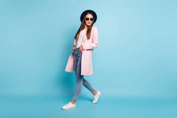 Photo of Full length photo of cute charming lady walking having promenade wearing pastel color topcoat denim jeans isolated over blue background