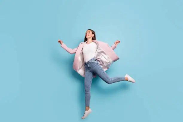 Photo of Full length photo of charming cute girl jump run for bargains on her holiday wear pink topcoat denim jeans isolated over blue background