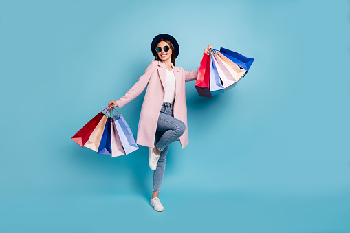 Full body photo of enthusiastic candid lady in eyewear, eyeglasses go shopping buy purchases wear pink coat denim jeans isolated over blue background