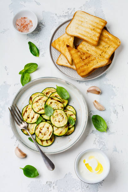 istock Grilled zucchini salad with basil leaves, yogurt sauce and fried bread in a simple ceramic plate on a white concrete background. Flat lay with copy space. 1171903219
