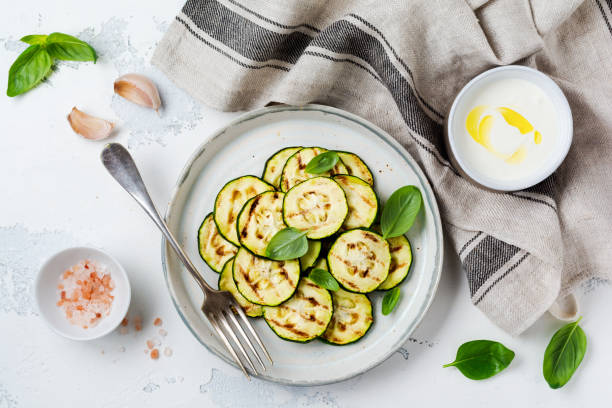 Grilled zucchini salad with basil leaves, yogurt sauce and fried bread in a simple ceramic plate on a white concrete background. Flat lay with copy space.