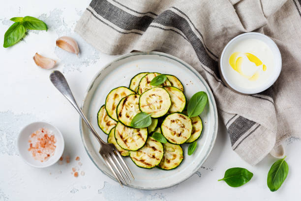 Grilled zucchini salad with basil leaves, yogurt sauce and fried bread in a simple ceramic plate on a white concrete background. Flat lay with copy space. stock photo