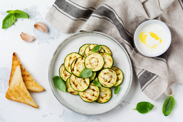 istock Grilled zucchini salad with basil leaves, yogurt sauce and fried bread in a simple ceramic plate on a white concrete background. Flat lay with copy space. 1171903379