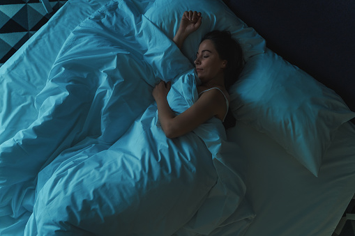 Young beautiful girl or woman sleeping alone in big bed at night, top view, blue toned.
