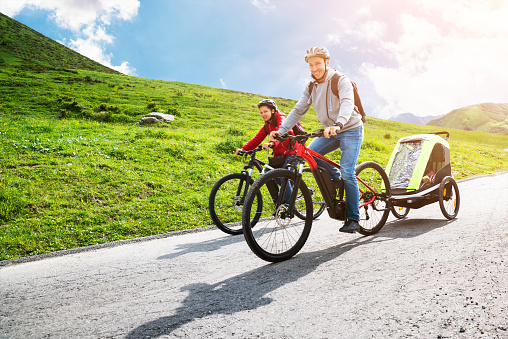 Family With Child In Trailer Riding Mountain Bikes In Alps