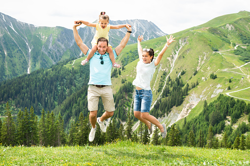 Happy Family With Little Girl Jumping In Austrian Mountains In Summer