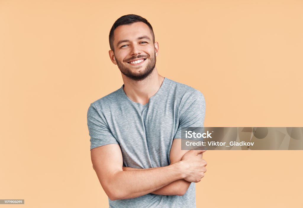 Glücklich lächelnd stattlichen Mann mit gekreuzten Armen Blick auf die Kamera über beige Hintergrund - Lizenzfrei Männer Stock-Foto