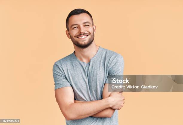 Glücklich Lächelnd Stattlichen Mann Mit Gekreuzten Armen Blick Auf Die Kamera Über Beige Hintergrund Stockfoto und mehr Bilder von Männer