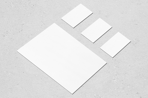 One empty white vertical a4 sized poster and three horizontal rectangle business card mockups with soft shadows on neutral light grey concrete background. Flat lay, isometric composition.