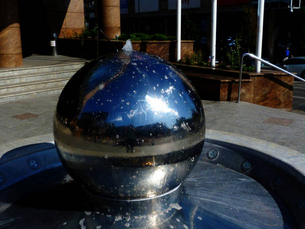 shiny stainless steel sphere fountain with strong reflection in urban setting with blurry background. summer and outdoors concept. urban living and lifestyle.