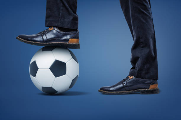 les hommes d'affaires géants jambes avec un pied restant sur un ballon de football le tenant en place. - business human foot shoe men photos et images de collection