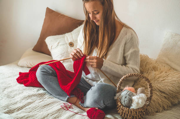 la belle fille tricote un chandail chaud sur le lit. le tricot comme passe-temps. accessoires pour tricoter. - tea cup cup shape red photos et images de collection