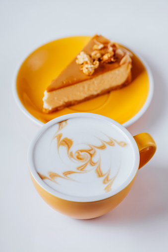 Cup of hot cappuccino coffee with cake on white table with copy space