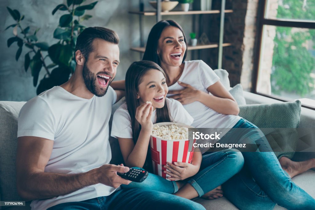 Portrait Of Nice Attractive Lovely Positive Glad Cheerful Cheery Family  Wearing Casual White Tshirts Jeans Denim Sitting On Sofa Having Fun  Watching Funny Video Enjoying Spending Free Time Stock Photo - Download