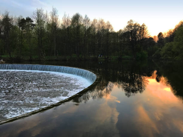 istock Tranquil lake with round cascaded waterfall and plain water reflecting the forest and sunset. Beautiful landscape background 1171926267