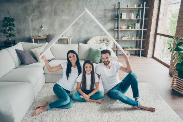 porträt von schönen attraktiven fröhlichen familie trägt lässige weiße t-shirts jeans sitzen auf teppichboden halten in der hand dach investition in industriellen loft stil interieur wohnzimmer gemütlichen komfort - joy of living stock-fotos und bilder