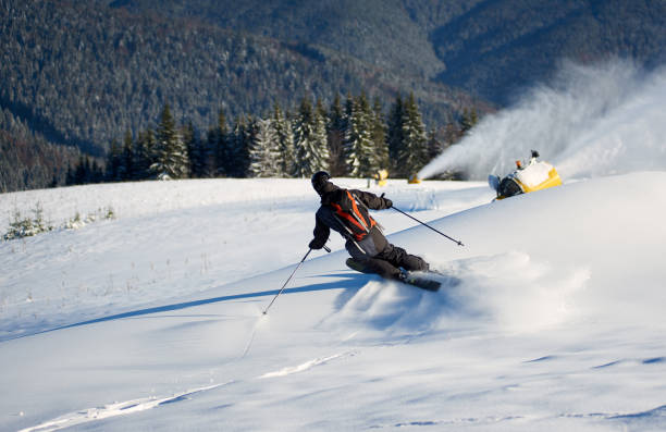 istock Man skiing on prepared slope with fresh snow. Snow gun machine making artificial snowfall. Magic nature on background. 1171927157