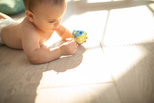 Baby boy in diaper crawling on floor and playing with his favorite toy at apartment