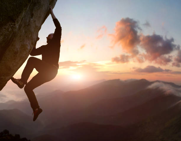 istock Rock climbing. Male climber trying staying on challenging rock, overcoming obstacles. Mountain and sunrise on background 1171928983