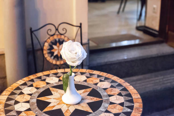 White rose in small ceramic vase on mosaic table at evening