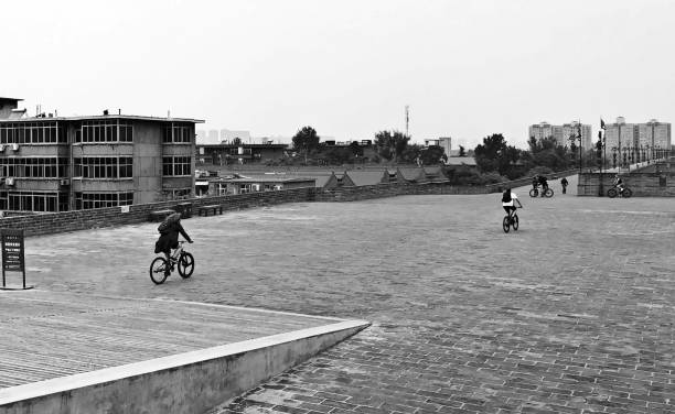 tourists biking through a chinese town square with old residentials buildings in shaanxi china. black and white - plattenbau homes architectural detail architecture and buildings imagens e fotografias de stock