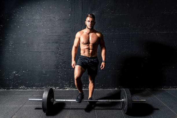 ジム暗いイメージの実在の人々でトレーニングトレーニング後に重いバーベル重量の上に立って大きな筋肉を持つ若い筋肉の汗男 - men muscular build abdominal muscle large ストックフォトと画像