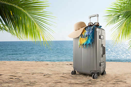 View of gray suitcase with pareo and hat on tropical beach