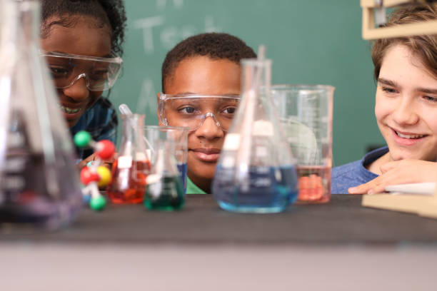 Junior high school age students conduct science experiments in classroom. Junior high, high school age students work on science experiments in school classroom setting.  STEM topics.  View through laboratory glassware. high school student child little boys junior high stock pictures, royalty-free photos & images