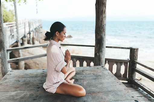 Young woman meditating in a yoga pose in a gazebo at the beach