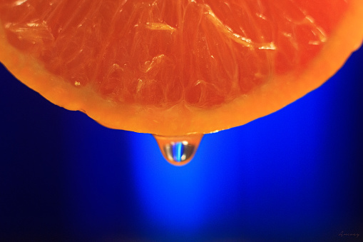 orange slice with juice drop and blue background