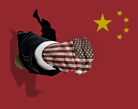 This is a conceptual photo of an American fist punching through a Chinese flag