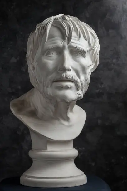 Photo of Gypsum copy of ancient statue Seneca head on dark textured background. Plaster sculpture man face.