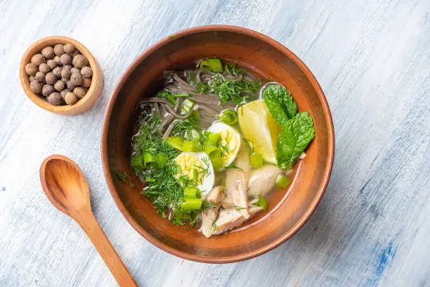 Photo of Top view tasty Vietnamese imperial soup with lemon, mint, herbs and buckwheat noodles, fish. Bowl with soup for lunch on blue background. Flat lay food photo. Seafood