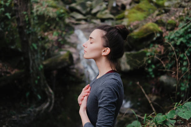 Photo of Young woman practicing breathing yoga pranayama outdoors in moss forest on background of waterfall. Unity with nature concept.