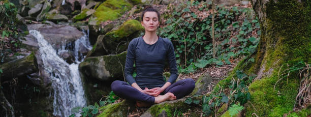 istock Young slim woman practicing yoga outdoors in moss forest on background of waterfall. Unity with nature concept. Girl meditates sitting 1171968888