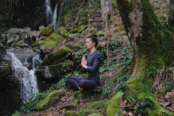 istock Young slim woman practicing yoga outdoors in moss forest on background of waterfall. Unity with nature concept. Girl meditates sitting 1171968892