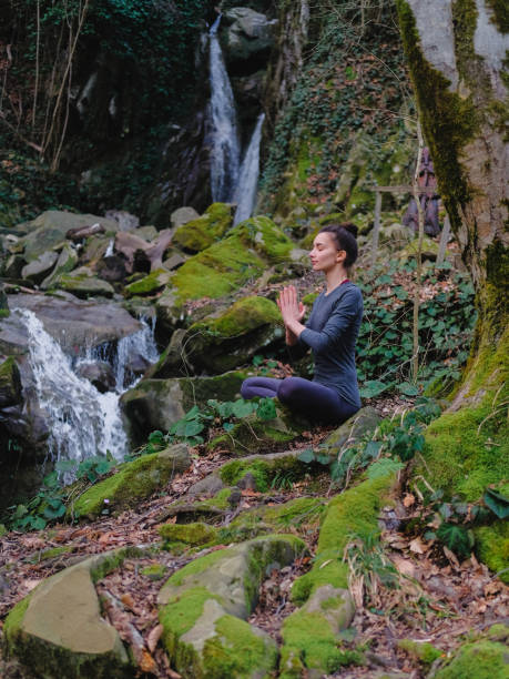 istock Young slim woman practicing yoga outdoors in moss forest on background of waterfall. Unity with nature concept. Girl meditates sitting 1171968907