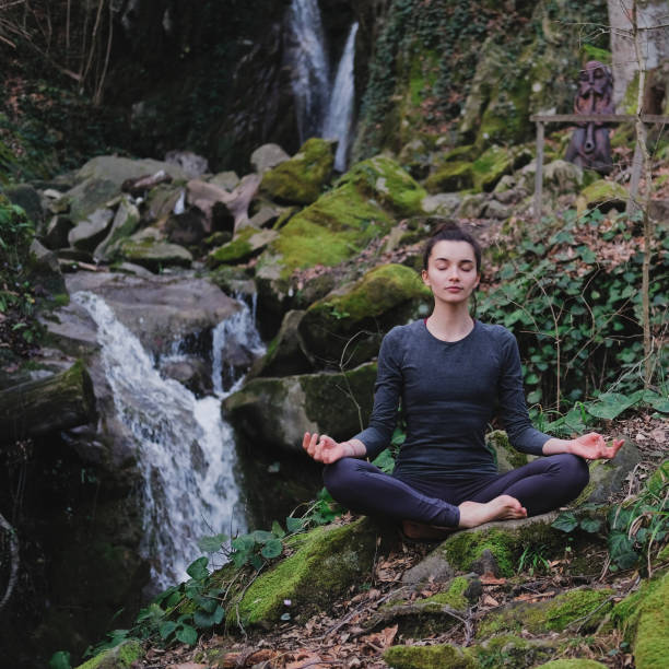 istock Young slim woman practicing yoga outdoors in moss forest on background of waterfall. Unity with nature concept. Girl meditates sitting 1171968915