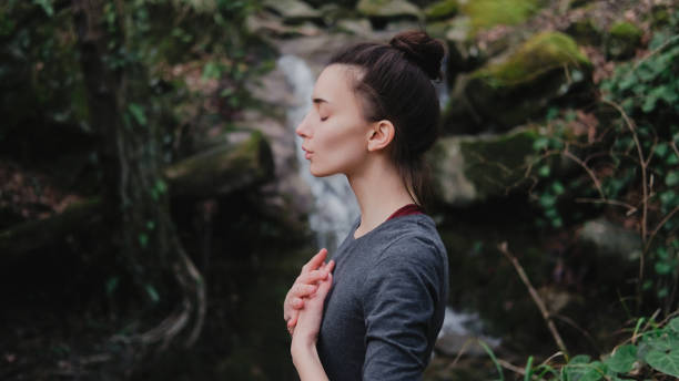 ioga de respiração praticando da mulher nova pranayama ao ar livre na floresta do musgo no fundo da cachoeira. unidade com conceito da natureza. - moss side - fotografias e filmes do acervo