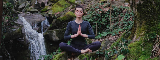 istock Young slim woman practicing yoga outdoors in moss forest on background of waterfall. Unity with nature concept. Girl meditates sitting 1171968928