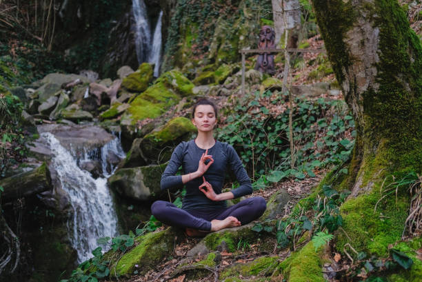 istock Young slim woman practicing yoga outdoors in moss forest on background of waterfall. Unity with nature concept. Girl meditates sitting 1171968934