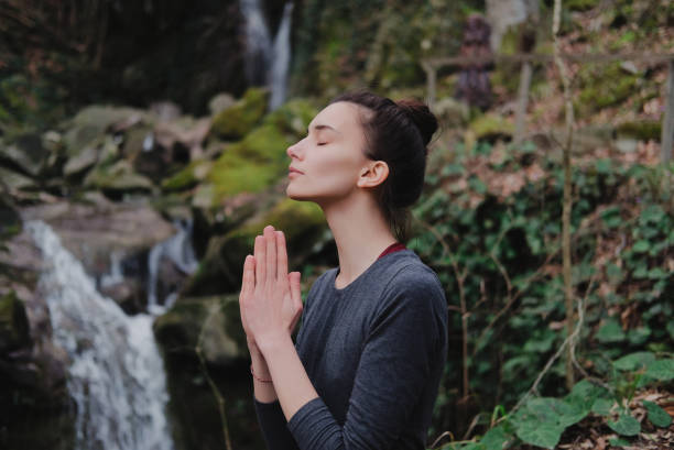 istock Young slim woman practicing yoga outdoors in moss forest on background of waterfall. Unity with nature concept. Girl standing with prayer hands 1171968939