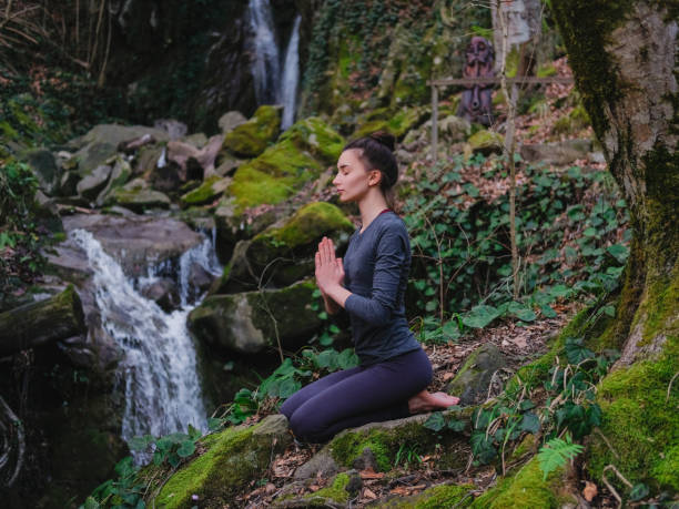 istock Young slim woman practicing yoga outdoors in moss forest on background of waterfall. Unity with nature concept. Girl meditates sitting 1171968941