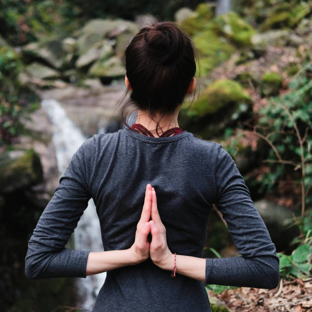 istock Young slim woman practicing yoga outdoors in moss forest on background of waterfall. Unity with nature concept. Girl standing with reverse prayer hands back 1171968945