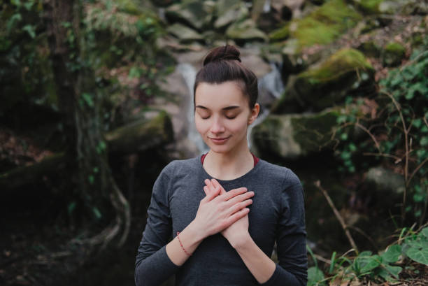 young woman practicing breathing yoga pranayama outdoors in moss forest on background of waterfall. unity with nature concept. - number of people human gender people waterfall imagens e fotografias de stock