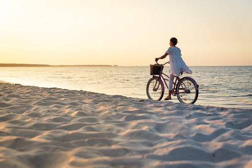 Woman with bike on beach at sunset